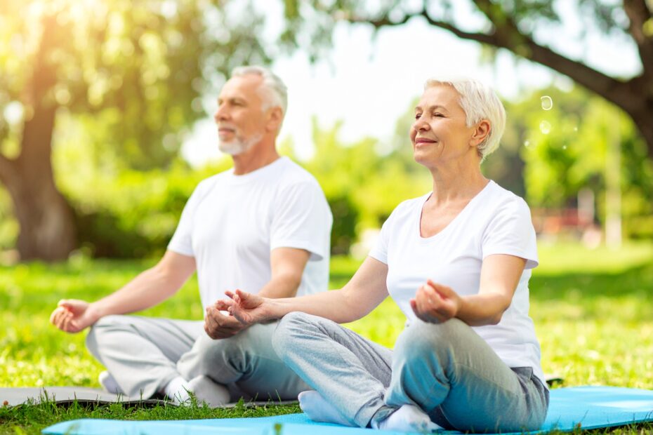 Elderly couple practicing mindfulness meditation outdoors on yoga mats in a sunny park.