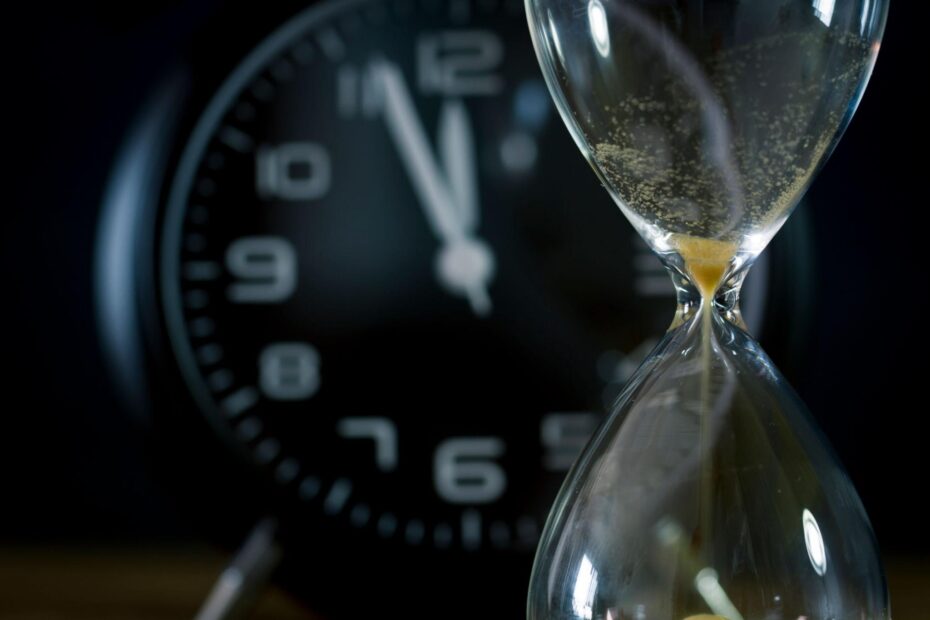 A symbolic image of a modern clock beside an hourglass with sand flowing, representing the contrast between measured time and the fleeting nature of life.